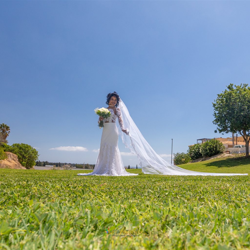 Bride with a long veil on a green lawn