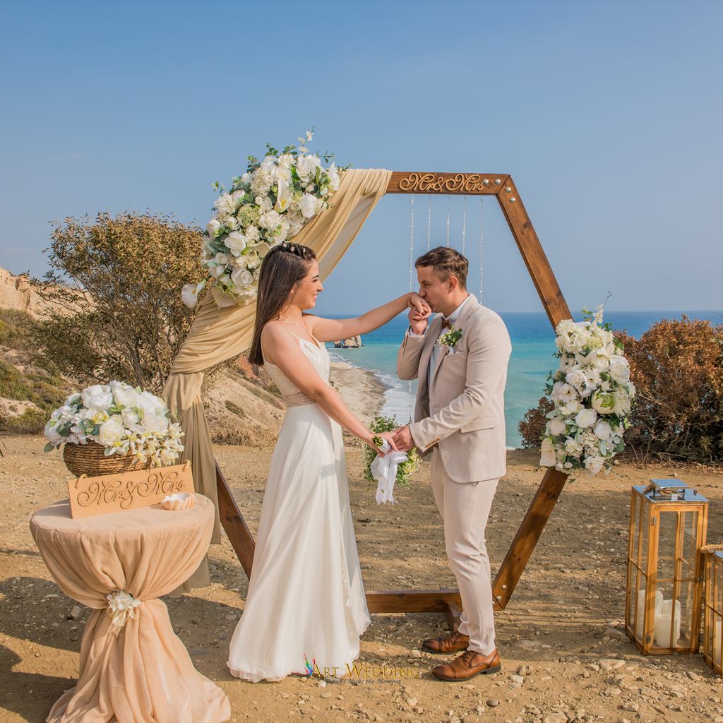 A kiss on the hand beside a wedding arch overlooking Petra tou Romiou