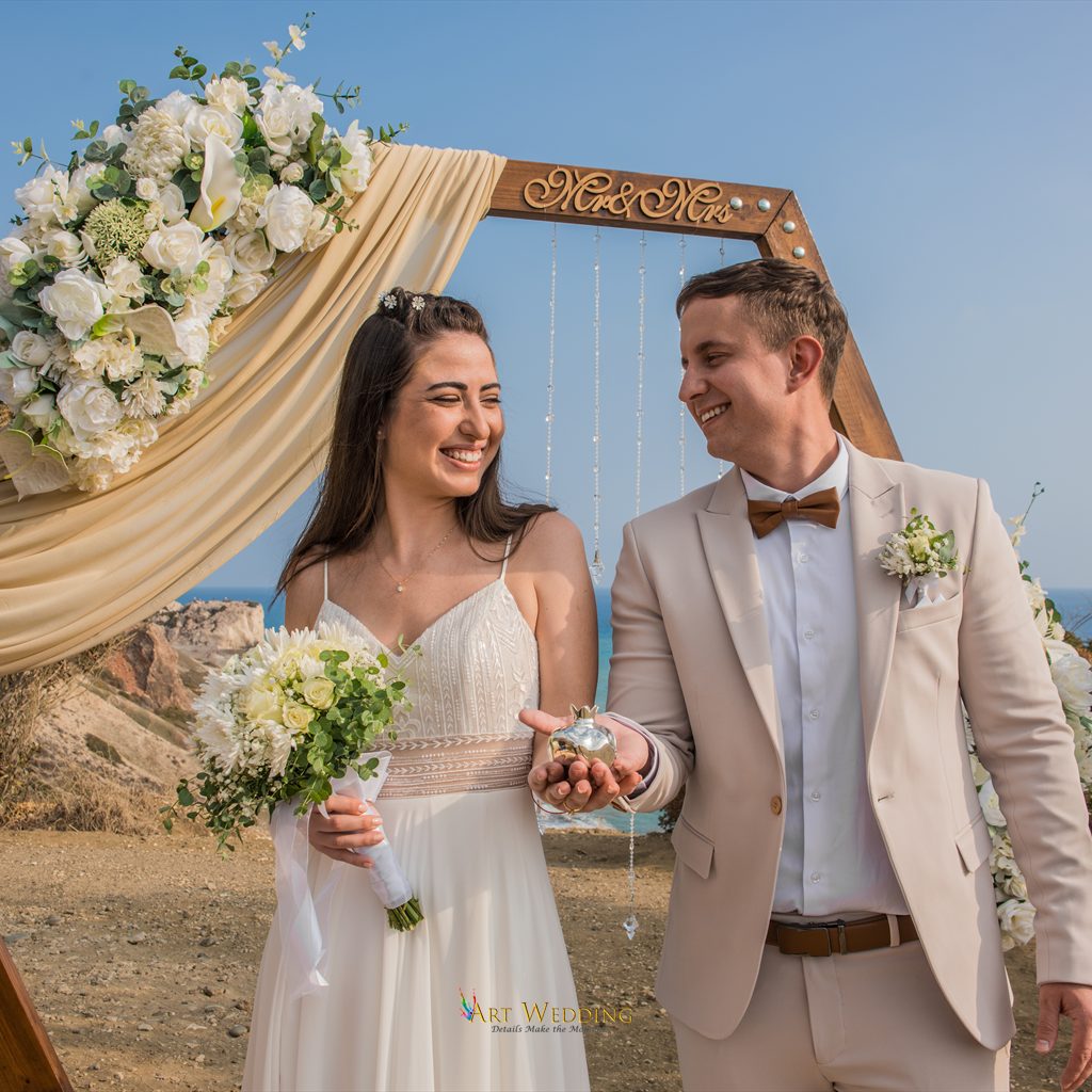 Newlyweds holding a bouquet and wedding gift beside the arch