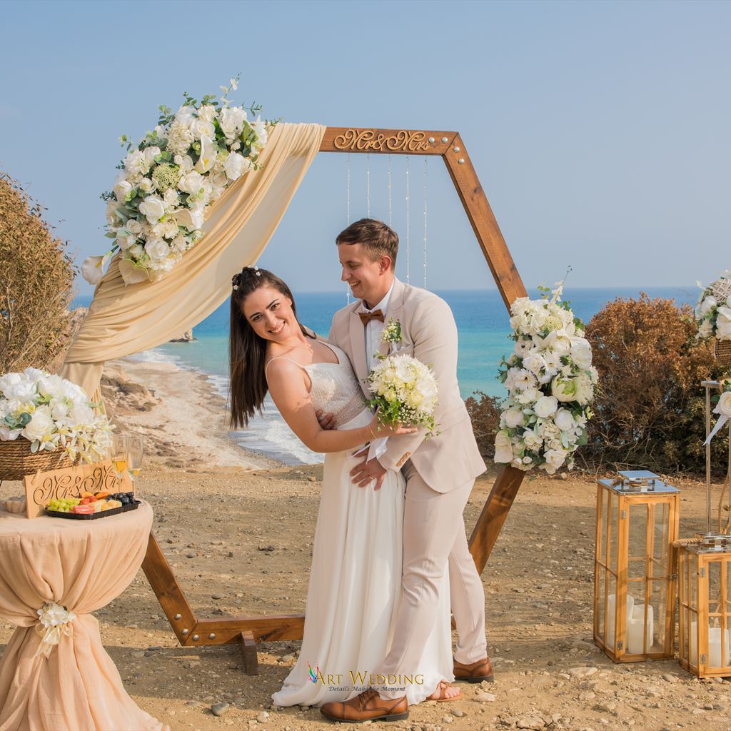 Smiling couple by an arch with white flowers above the sea
