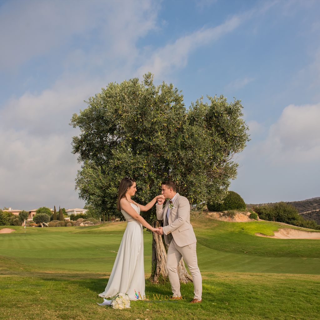 Groom kissing the bride’s hand beside an olive tree