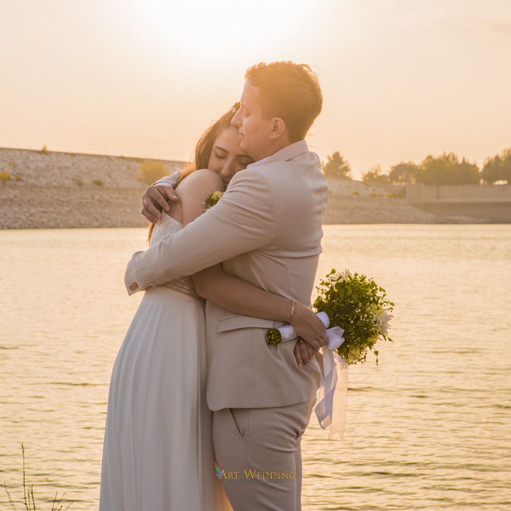 Newlyweds embracing by the water in golden sunset light