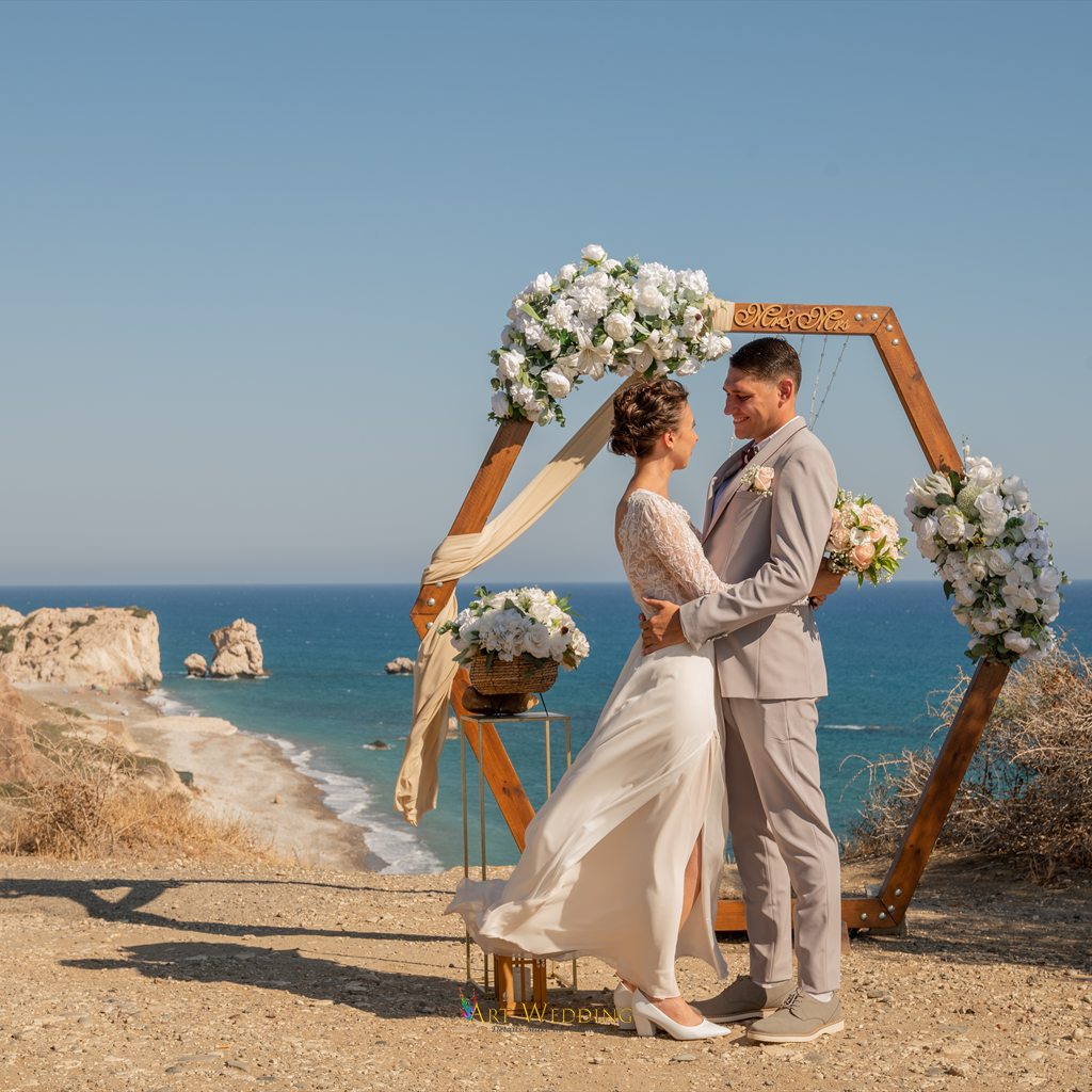 Newlyweds by a hexagonal arch with Aphrodite’s Rock in the background
