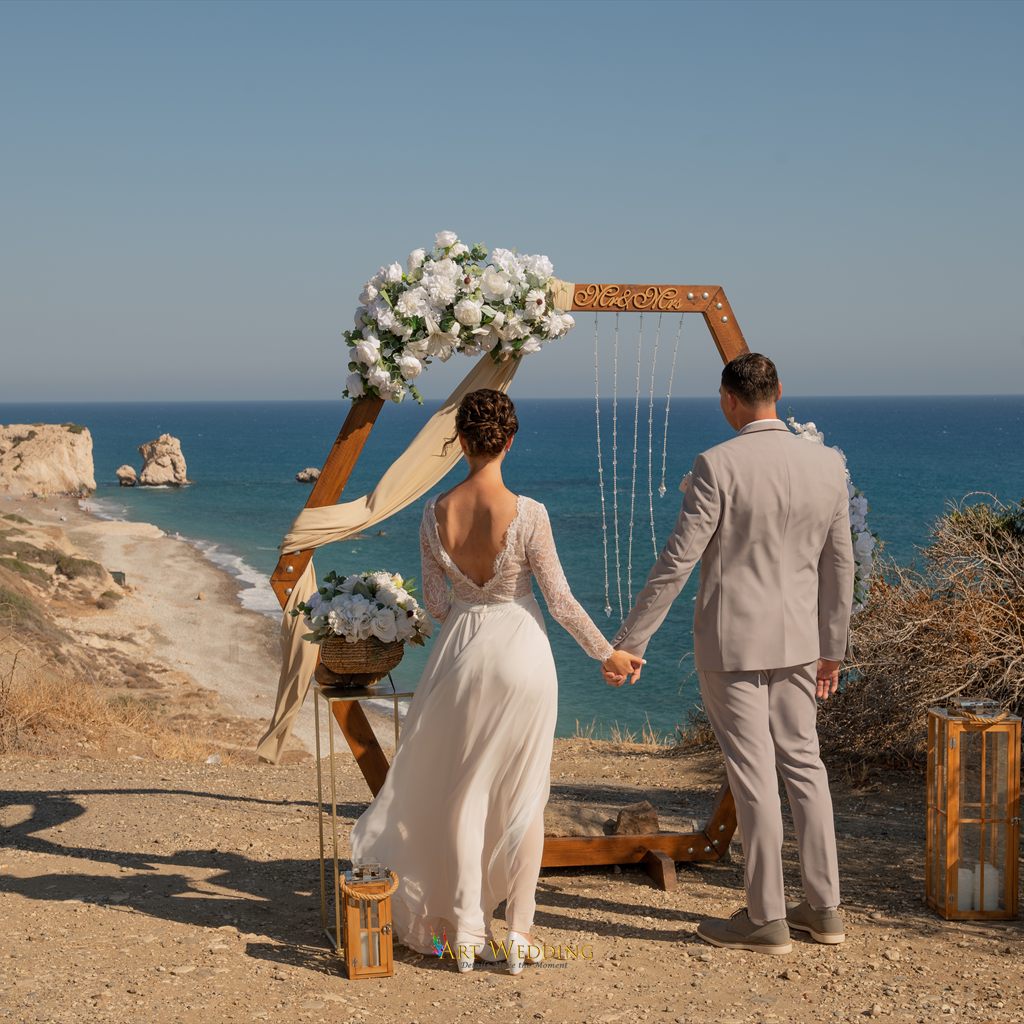 Newlyweds holding hands facing the arch and sea panorama