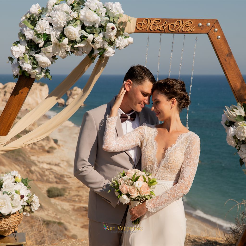 Bride and groom under a floral arch by the sea at Aphrodite’s Rock