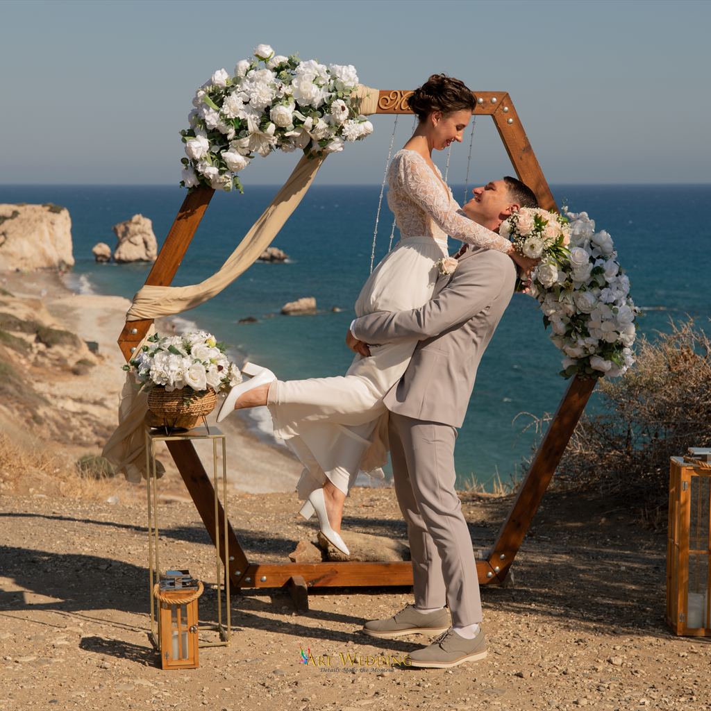 Groom lifting the bride beside a wooden arch above the sea