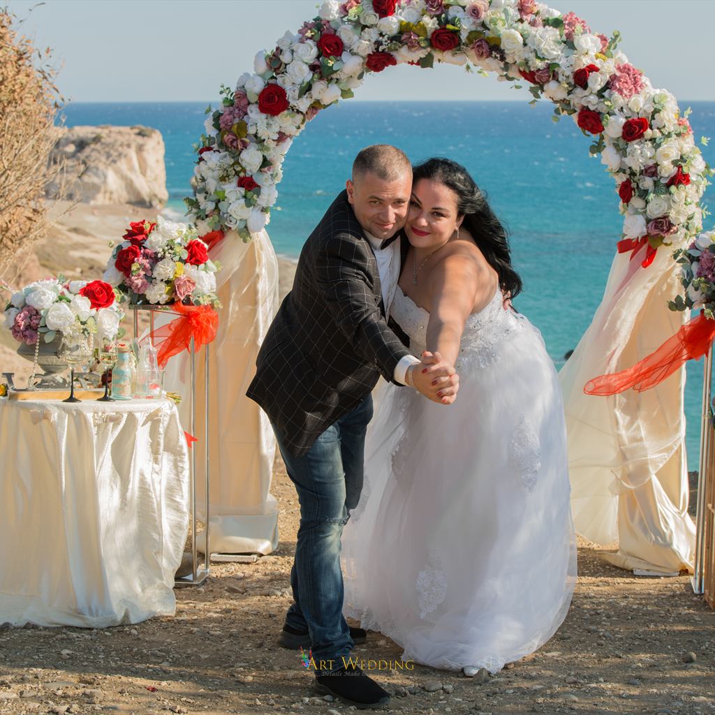Newlyweds beneath a round floral arch overlooking the sea