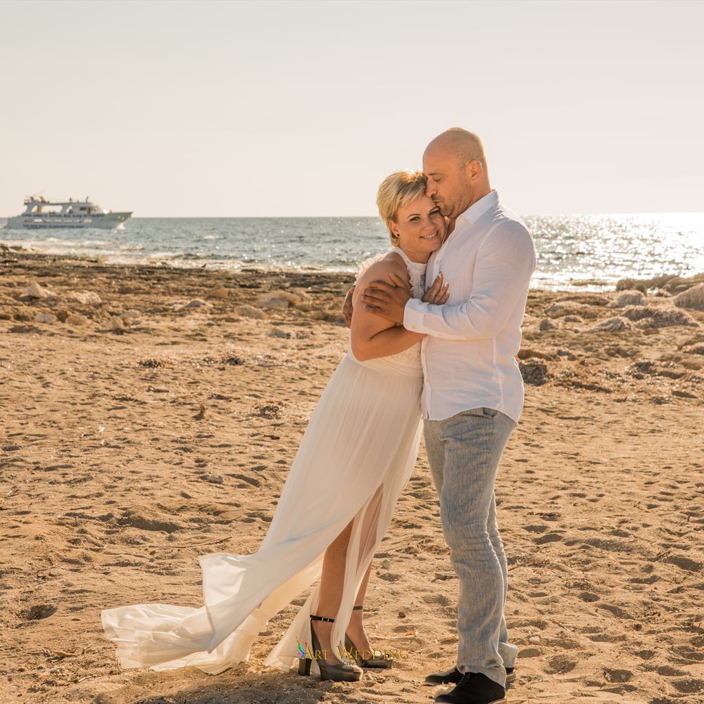 Smiling bride in the groom’s arms on the rocky beach