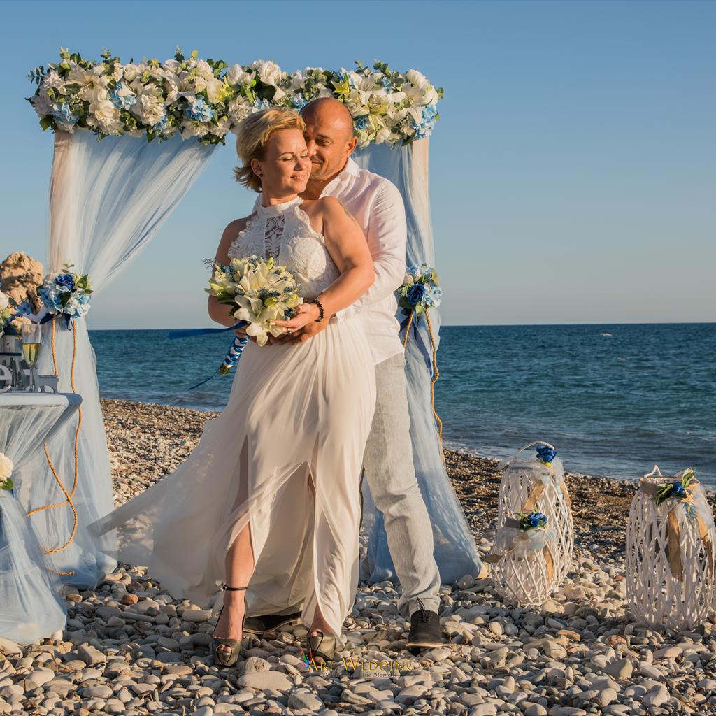 Newlyweds embracing beside their beach wedding arch