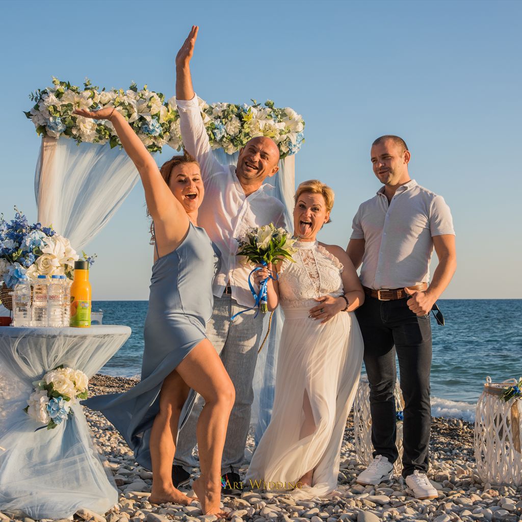 Newlyweds and guests beside a blue wedding arch on the beach