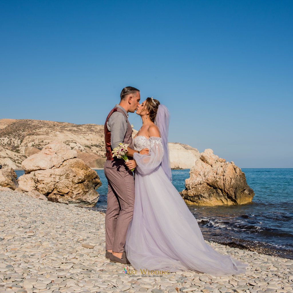 Newlyweds kissing on the beach beside sea rocks
