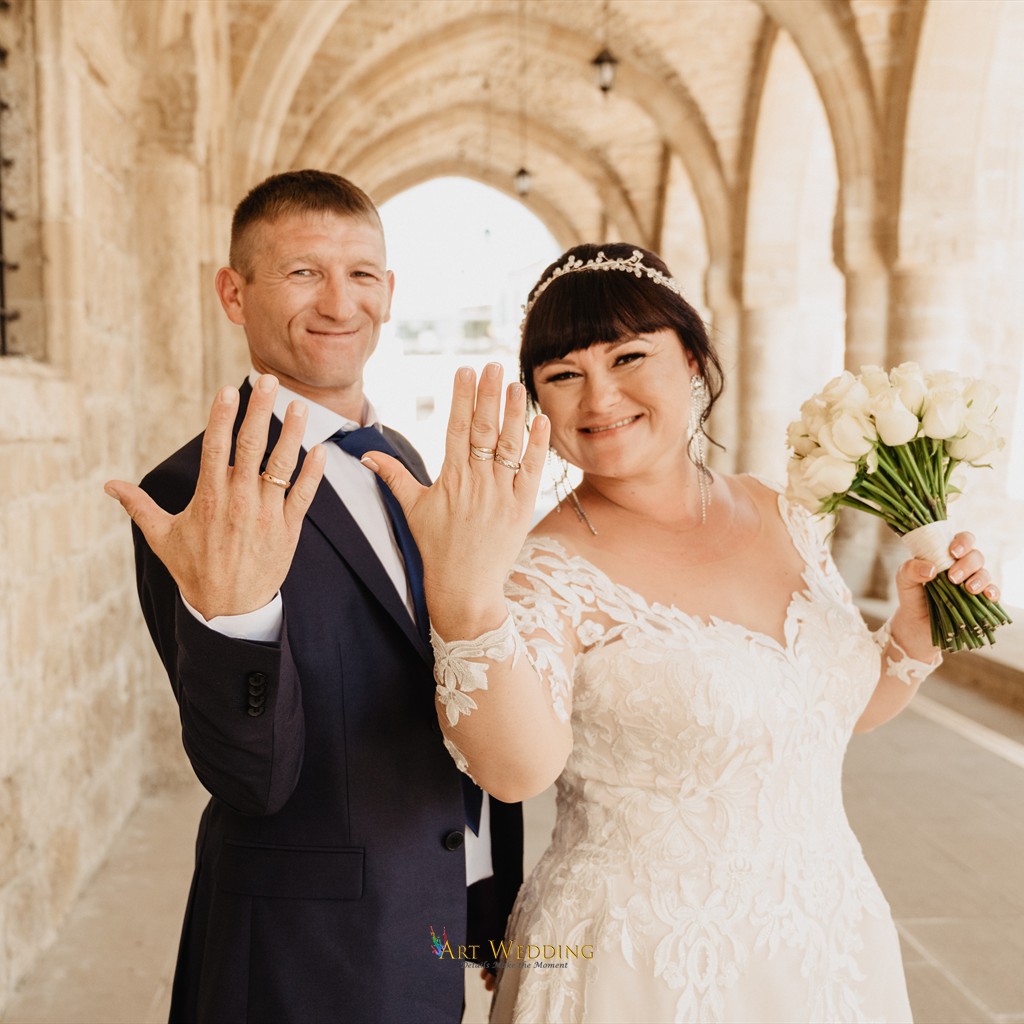 Newlyweds showing wedding rings beneath stone vaults