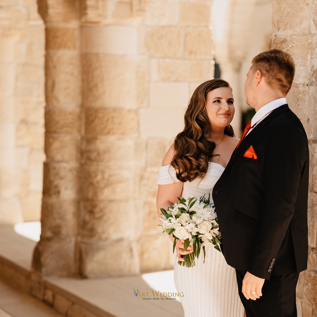Newlyweds with a white bouquet beside stone columns
