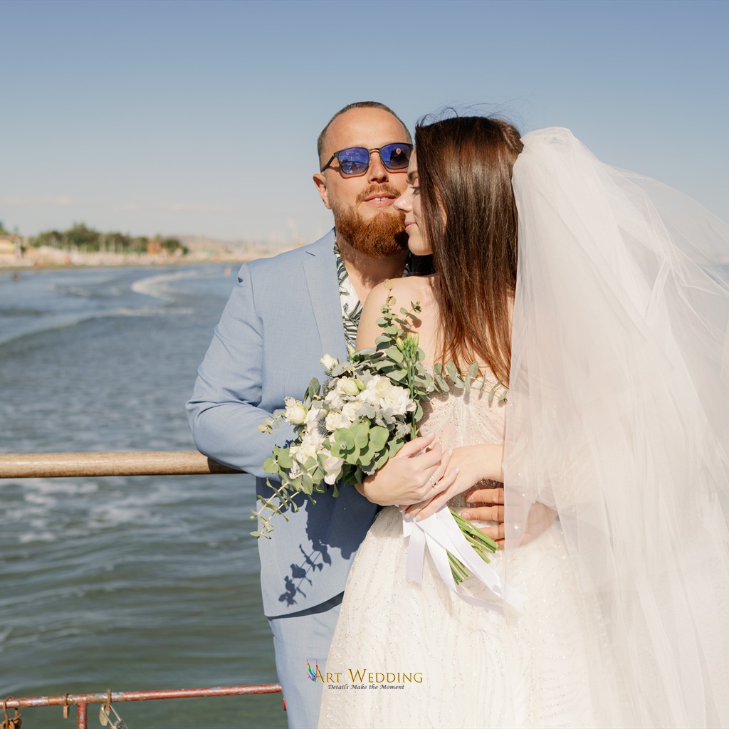 Newlyweds with a bouquet and veil by the sea