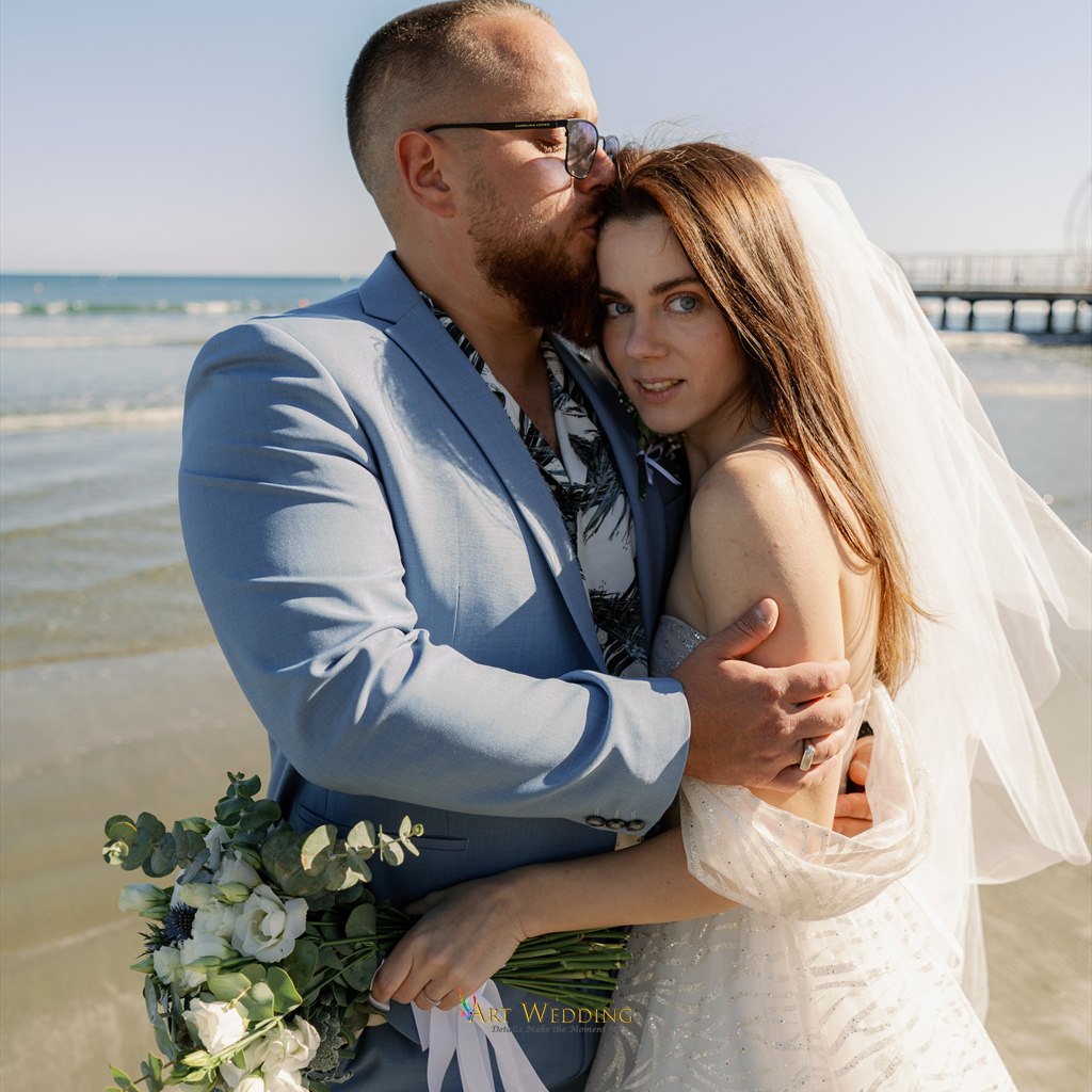 Groom kissing his bride on the forehead by the sea