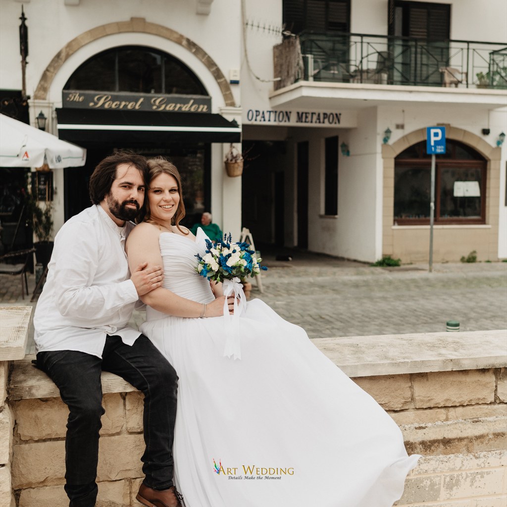 Newlyweds with a bouquet seated on a stone wall