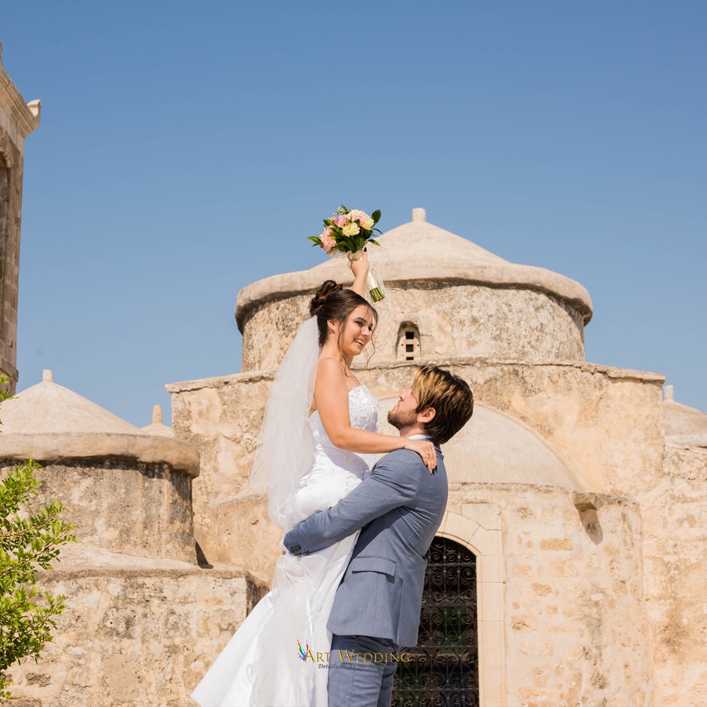 Bride holding her bouquet in the groom’s arms by an old church