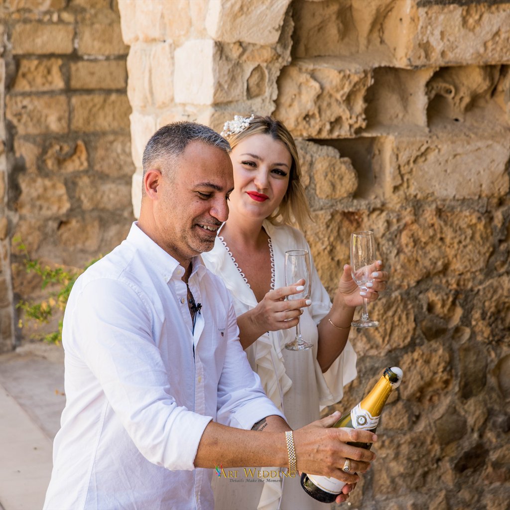 Groom opening champagne by a stone arch