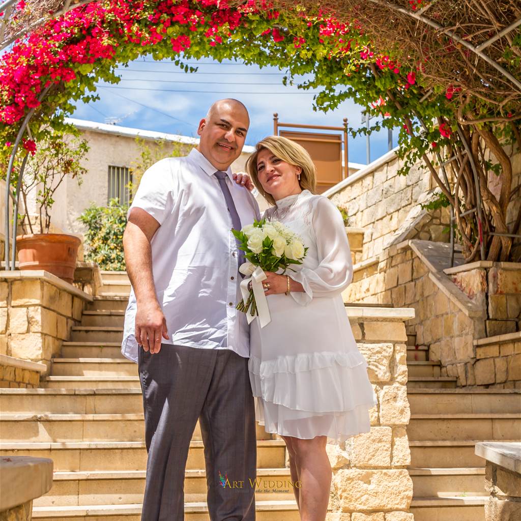Couple with a white bouquet beneath a flowering arch
