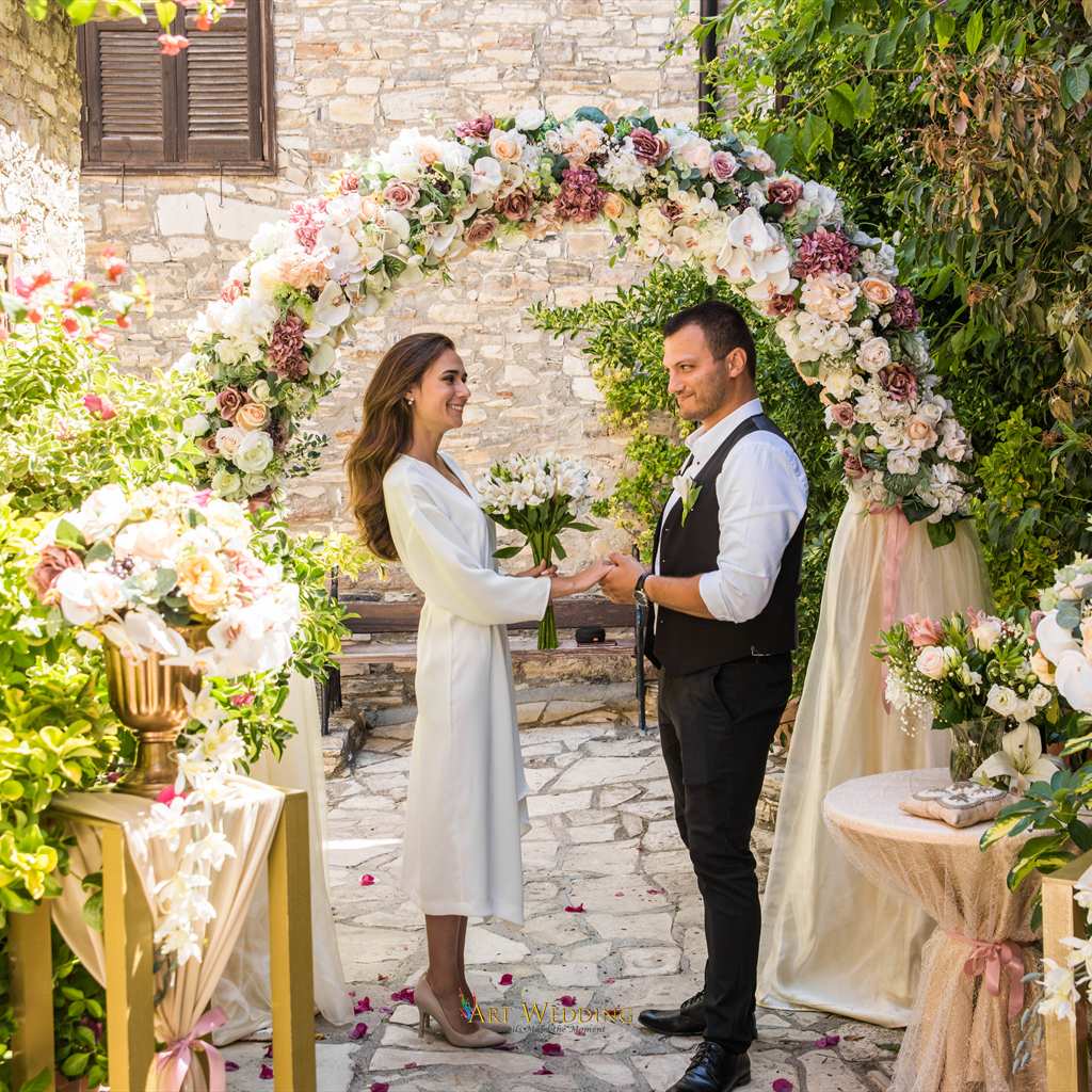 Bride and groom holding hands beneath a floral arch — Lefkara, Cyprus
