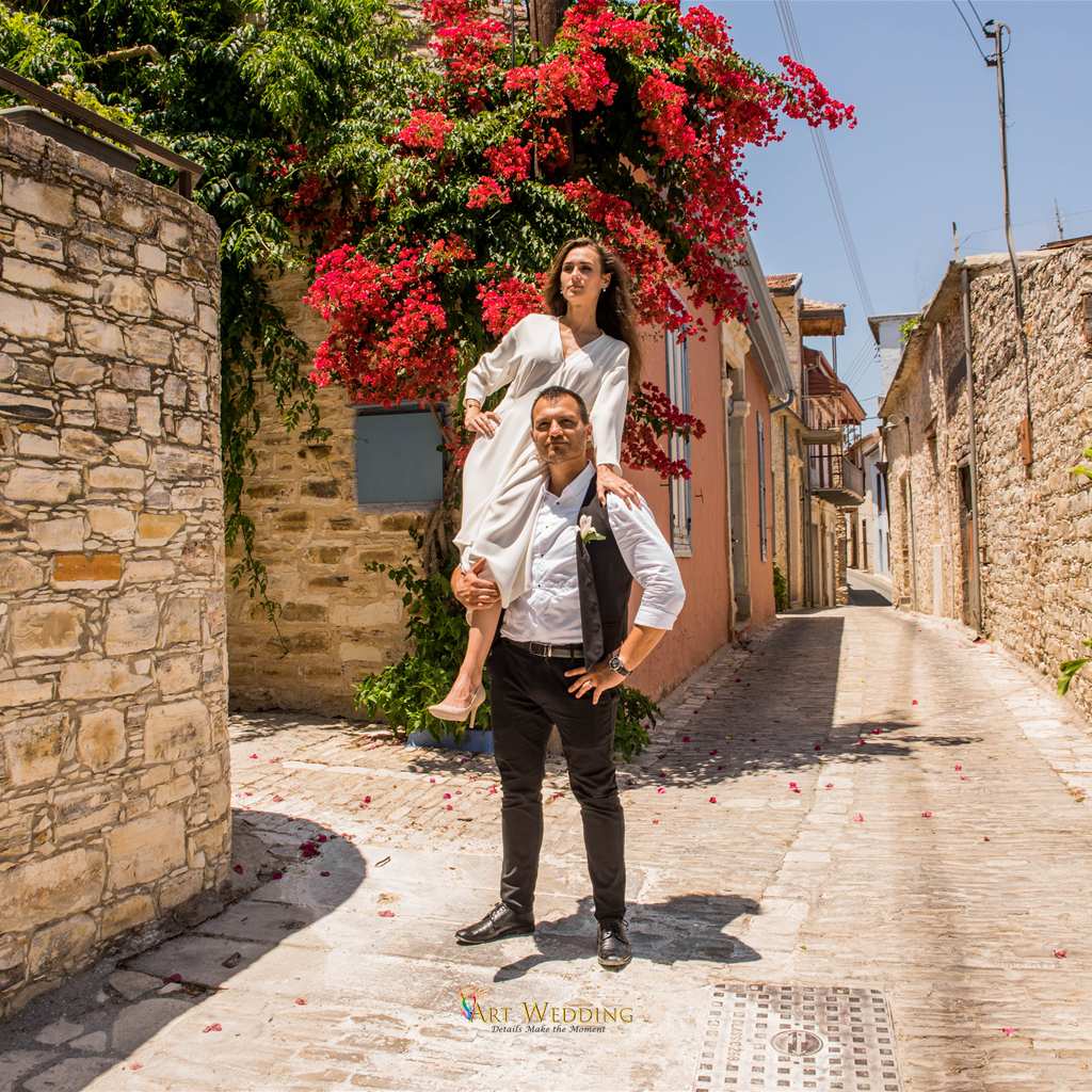 Groom carrying the bride on his shoulders beside bougainvillea — Lefkara, Cyprus