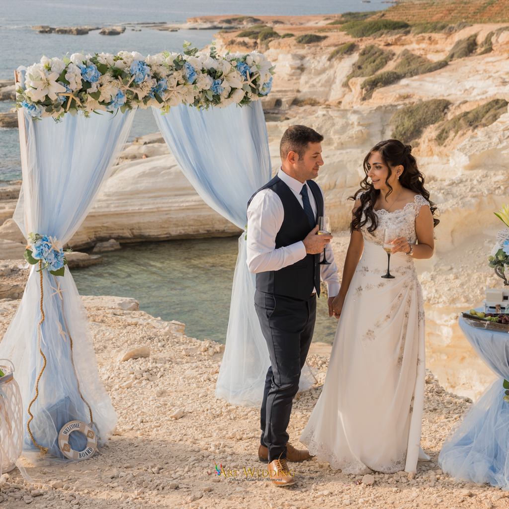 Newlyweds holding glasses beneath the wedding arch