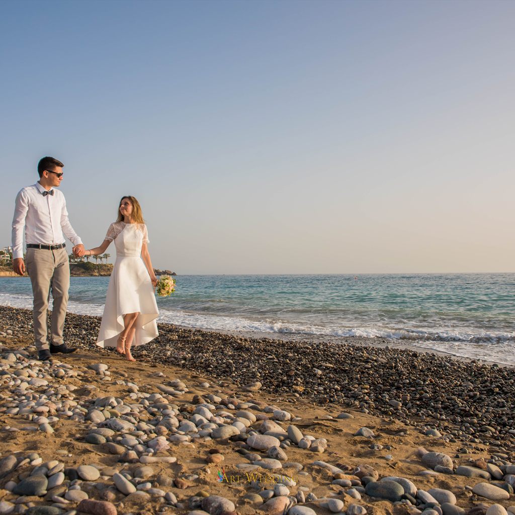 Newlyweds walk hand in hand on a pebble beach