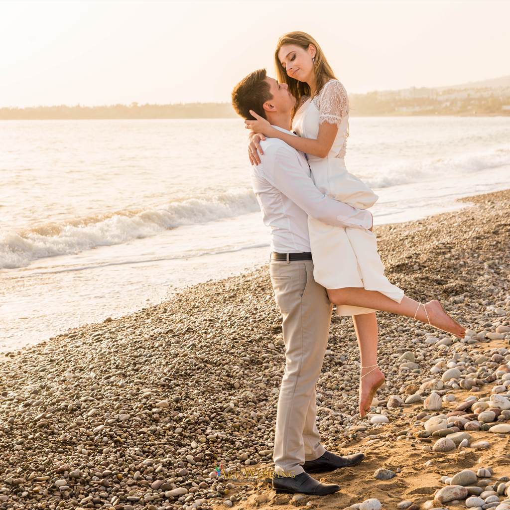 Groom lifts the bride on a pebble beach